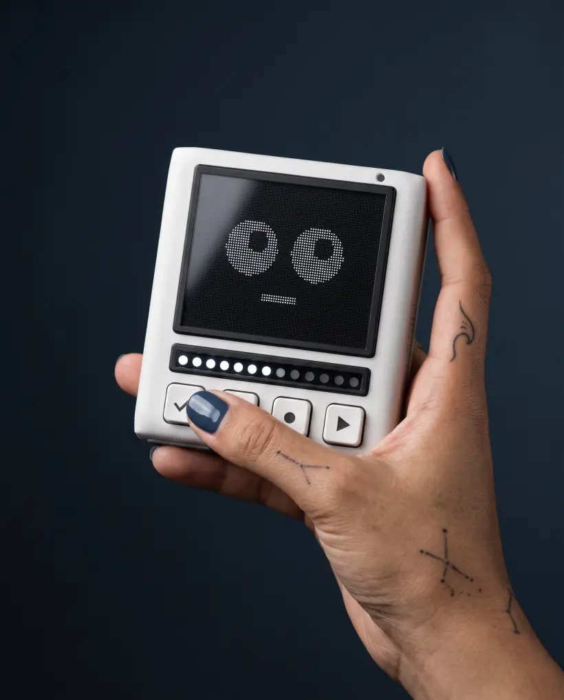 The Pixli held up at an angle in one hand against a dark background, its idle face lit